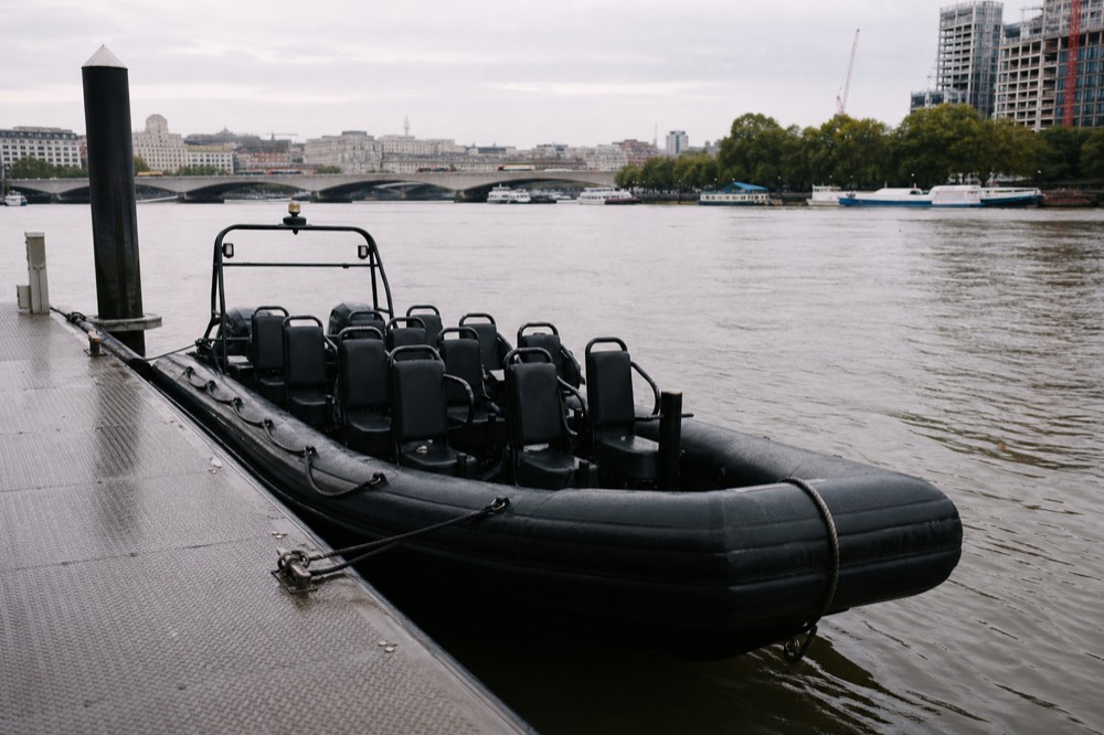 An empty twelve-seat rigid inflatable boat tied alongside a pontoon, rows of moulded seats and grab rails under grey morning light
