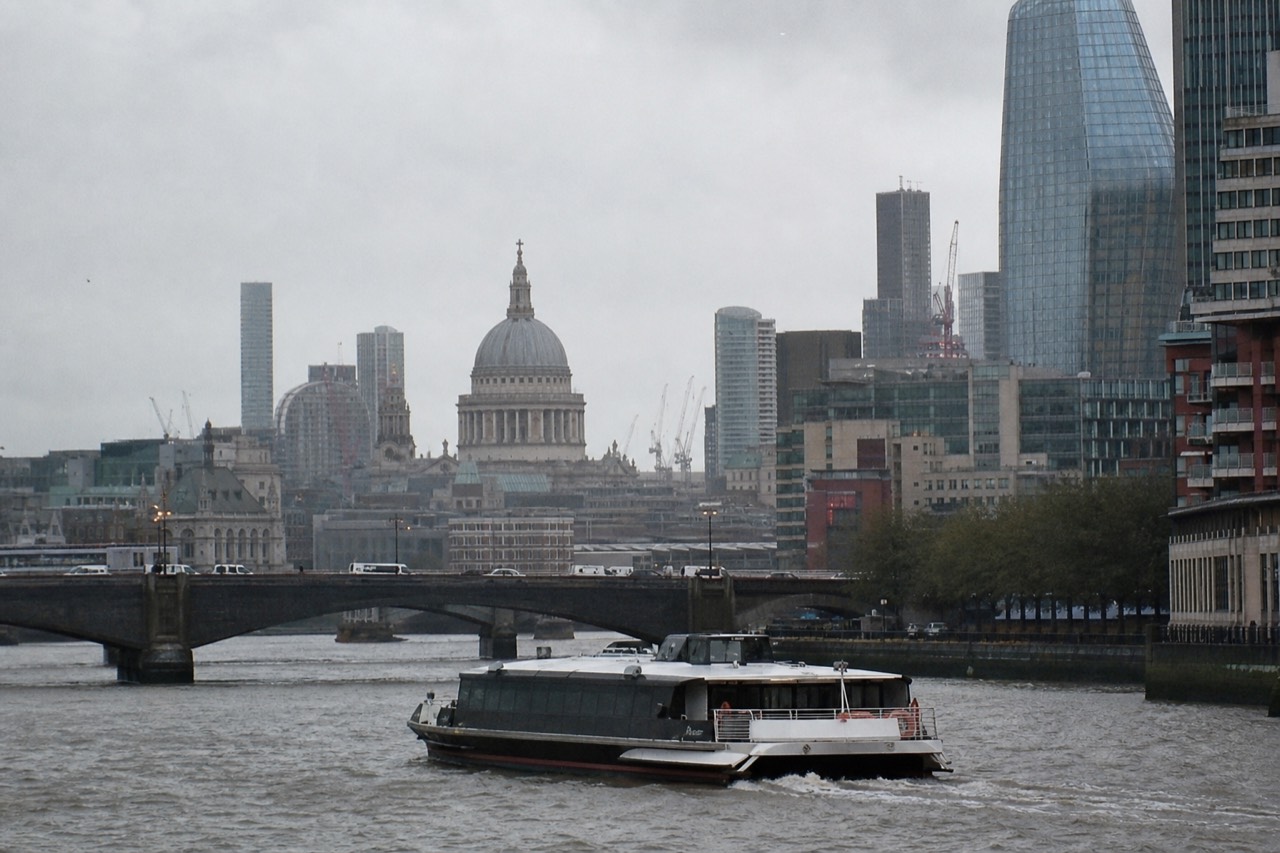 A river sightseeing boat mid-stream on a grey afternoon with the dome of St Paul's and City towers rising along the north bank