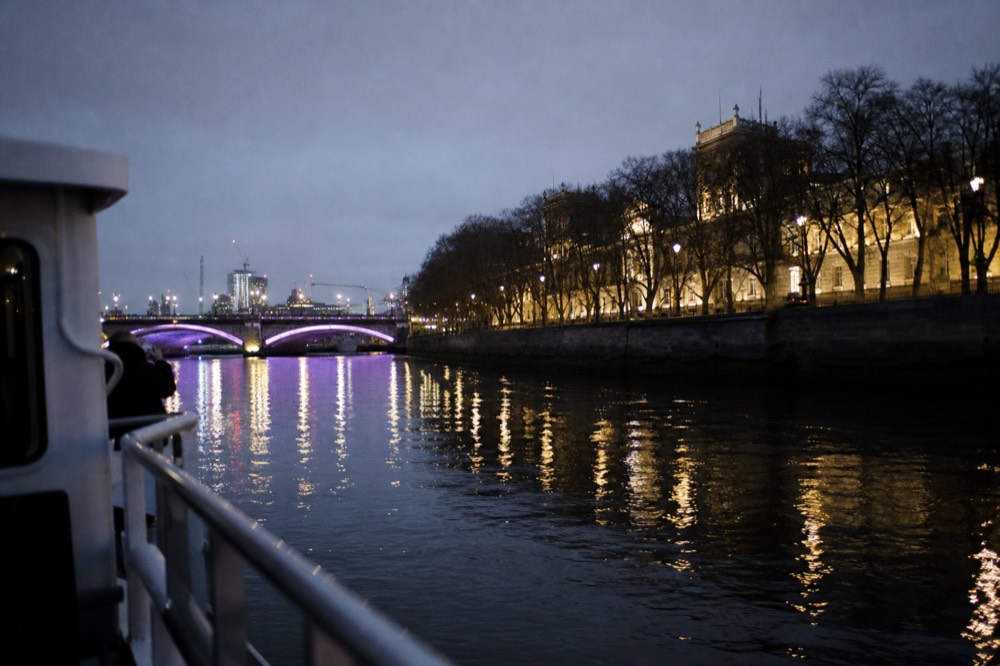 The lit Embankment and a floodlit bridge reflected in flat black water on a clear evening, boat rail in the foreground