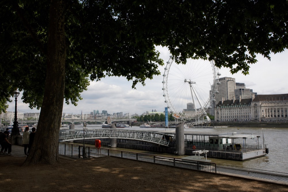 A floating pier pontoon on the south bank with its walkway curving down from the riverside promenade, a big wheel structure rising behind