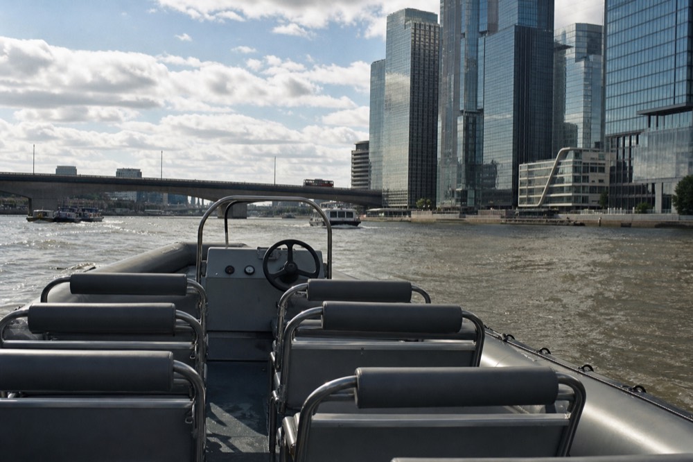 The empty bench seating of a small open river boat photographed from the stern on a bright day, grey tubes and a bare wheel console
