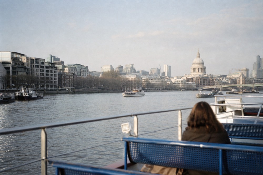 The open upper deck of a river boat with bench seats and a low rail, wide river and a dome on the far bank in afternoon sun
